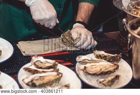 Chef In White Gloves Shucking A Fresh Oyster With Knife.