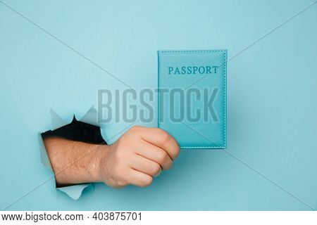 Traveler Tourist Man Hand Hold Passport From A Torn Hole In Blue Paper