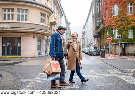 Happy Senior Couple Walking Outdoors On Street In City, Carrying Shopping Bags.