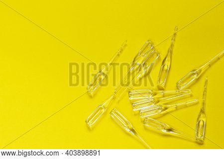 Ampoules On A Yellow Background. A Group Of Medical Ampoules. Glass Ampoules Scattered On A Corrugat