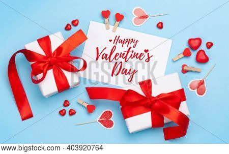 Valentines day greeting card. Gift boxes, heart decor and candy sweets over blue background. Top view flat lay