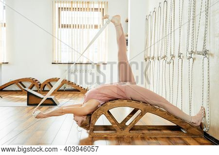 Mature Woman Doing Stretching Exercises On Yoga Backbend Bench In Studio