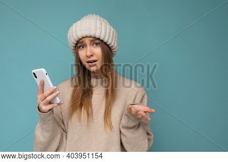 Photo Of Beautiful Asking Upset Young Blonde Woman Wearing Stylish Beige Warm Sweater And Knitted Wi
