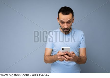 Photo Of Amazed Handsome Young Man With Beard Wearing Everyday Blue T-shirt Isolated Over Blue Backg