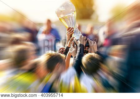 Children Holding Trophy Cup Above Heads In A Stadium. Group Of Happy Boys Rising Golden Cup After Wi