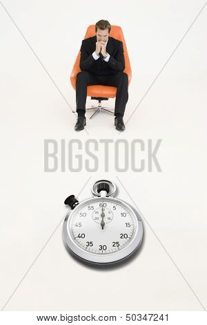 Anxious businessman sitting on chair with stopwatch in front of him representing loss of time