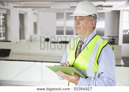 Middle-aged man in reflector vest and hard hat with clipboard at office