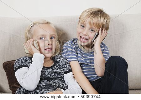 Happy brother and sister using cell phones at home