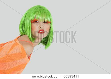 Portrait of young woman wearing green wig over gray background