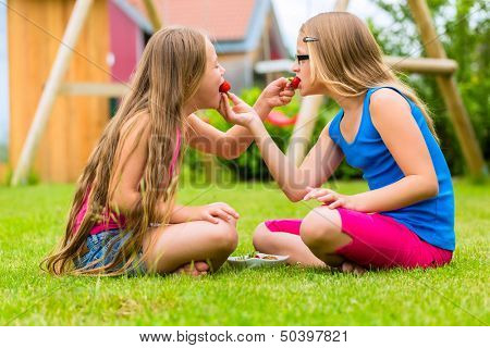 Happy Girls or sisters playing at home in garden and eating strawberries