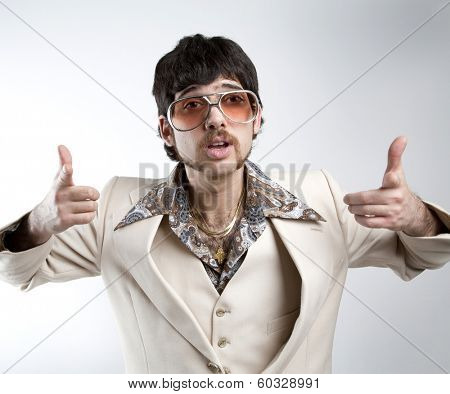 Portrait of a retro man in a 1970s leisure suit and sunglasses pointing to the camera 