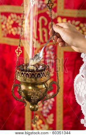 Hand adding incense chunks into a burning incense thurible