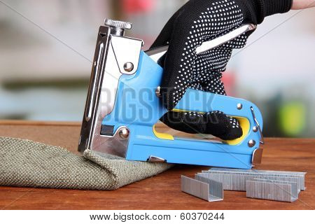 Fastening fabric and board using construction stapler on bright background