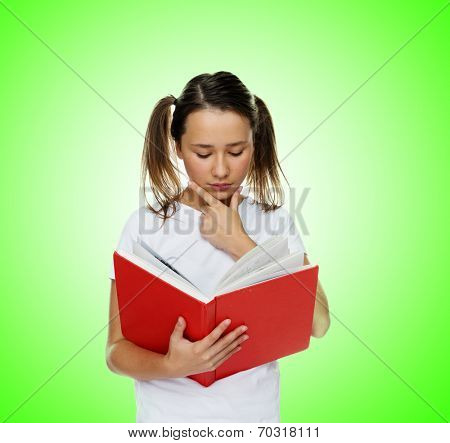 Smart cute girl with twintail hairstyle and a pensive facial expression reading from a red book, portrait on green
