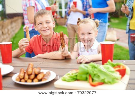 Children eating grilled sausages at family village