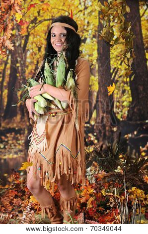 A beautiful Indian teen carrying an armload of corn.  She's in a colorful  fall setting.