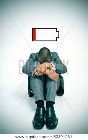 a young businessman curled up in the floor with his head between his knees and an illustration of a low battery