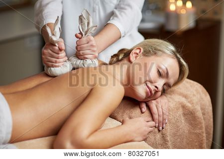 people, beauty, spa, healthy lifestyle and relaxation concept - close up of beautiful young woman lying and having herbal bag massage in spa