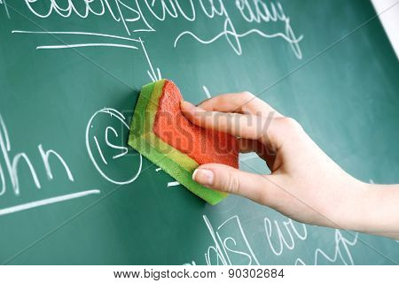 Teacher hand wiping off sentences from blackboard background