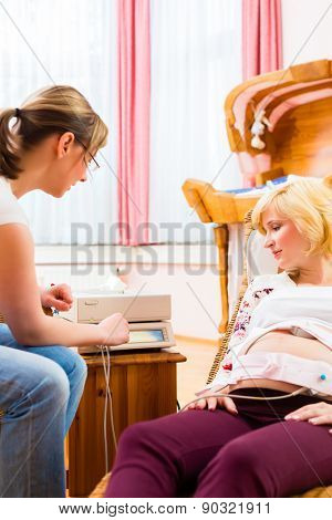 Midwife exanimating belly of pregnant woman with CTG scanning in practice