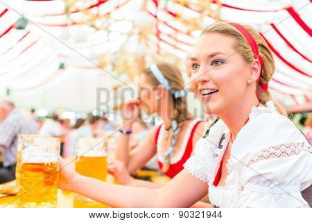 Women drinking Bavarian beer in tent on Oktoberfest or dult wearing dirndl