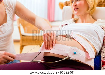 Midwife exanimating belly of pregnant woman with CTG scanning in practice