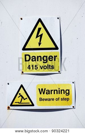 High voltage danger warning sign for 415 volts of electricity with an additional warning to beware of a step below mounted on a white wall