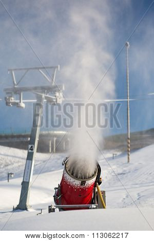 Snow-machine bursting artificial snow  over a skiing slope to alow for the skiing season to start