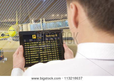 Businessman with tablet in airport with flight schedule and departure and gate information