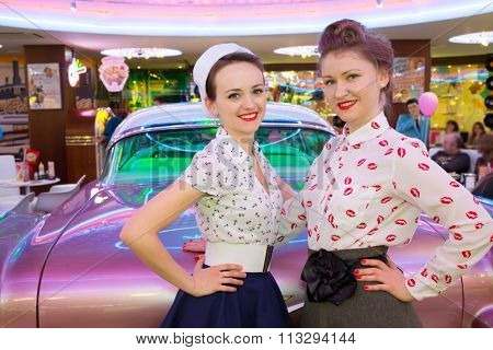 Two beautiful young girls in retro dress have a fun at the bar with pink car.