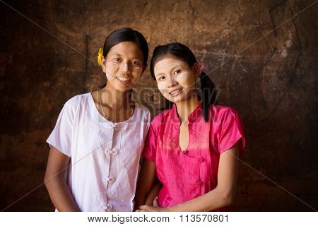 Portrait of two beautiful Myanmar girls smiling, low light inside a temple.
