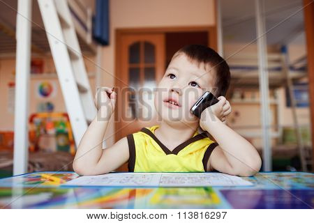 Little boy takes an important call on his cell phone, while drawing at home with felt pens.