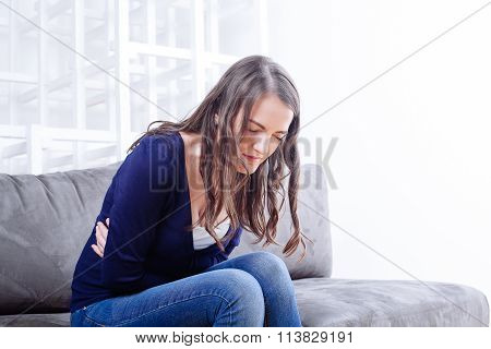 Young Woman Sitting On Sofa Suffering From Stomach Ache