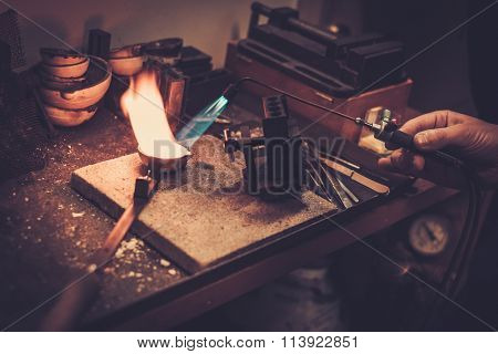 Goldsmith melting gold to liquid state in crucible with gasoline burner.