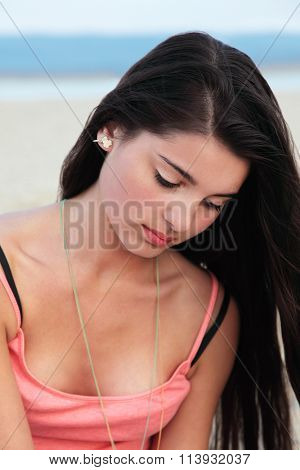 Beautiful young european teenage girl with long dark hair looking down in a thoughtful mood.