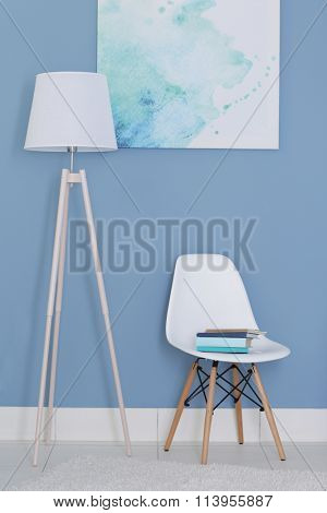Room design with white floor lamp, chair and picture over blue wall