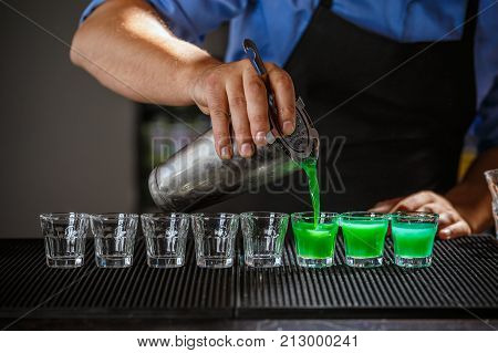 Barman pouring hard spirit into glasses on bar counter