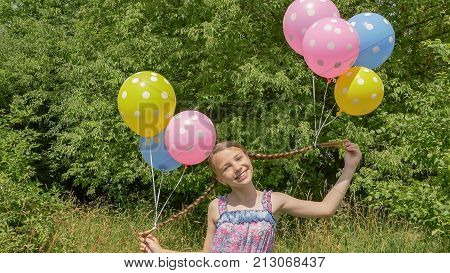Cheerful and pretty girl with colorful balls attached to her hair and braids on her head. Funny idea with balloons