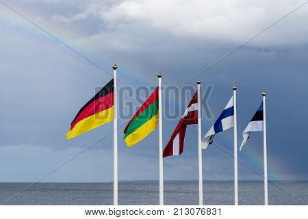 Estonian Finnish Lithuanian Latvian and German flags waving in the wind blue sky and rainbow in the background
