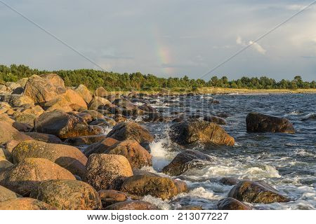 Boulders forest shore evening light sunset clouds blue sky and rainbow on the Baltic Sea. Mohni small island in Estonia Europe.