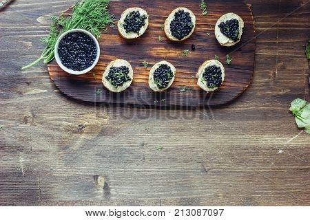 Top view of black caviar appetizers at wooden board