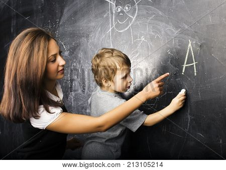 little cute boy in glasses with young real teacher, classroom studying at blackboard school kido