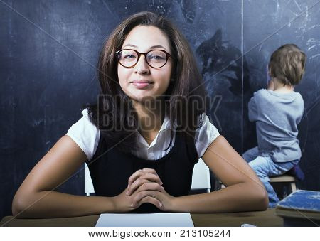 little cute boy in glasses with young real teacher, classroom studying at blackboard school kido