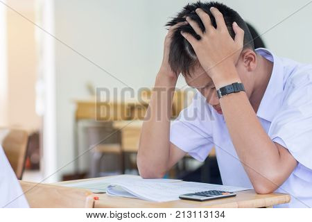 Asian boy student studying stressed headaches for test or exams in classroom learning lessons doing final exam at high school with Thailand uniform in class room. Education system concept.
