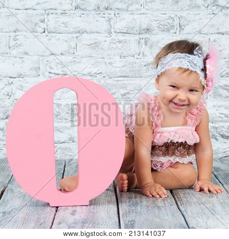 Beautiful and cute girl in a pink dress with the letter O. Emotional girl