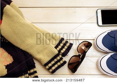 Winter clothes ;blues neaker ,glasses ,sweaters and smartphone on white wood board background ,concept idea for traveling in winter