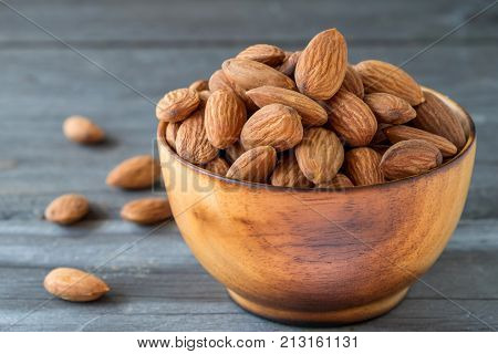 Almonds in wooden bolw on wooden floorCups of wood have burn marks.with almons laid around wood bolw.