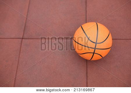 Basketball, a bright, new ball lies on the red, rubber coating of the stadium.
