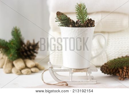Winter Concept With White Blanket Pullover, Gloves, Sleds, Cup, Cones And Fir Branches.
