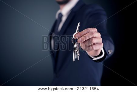 Young businessman hand over keys with empty dark background